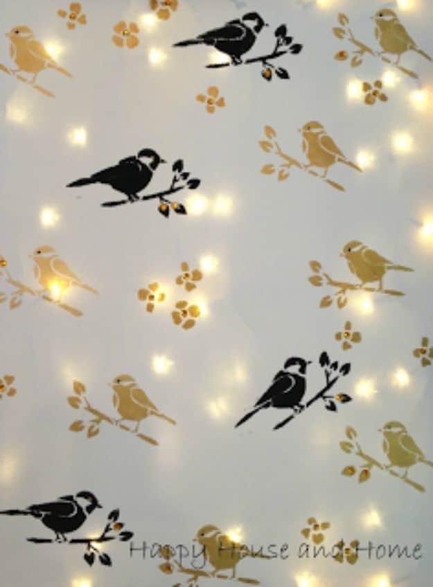 Canvas stenciled with black and gold birds on branches, lit from behind by small warm twinkle lights