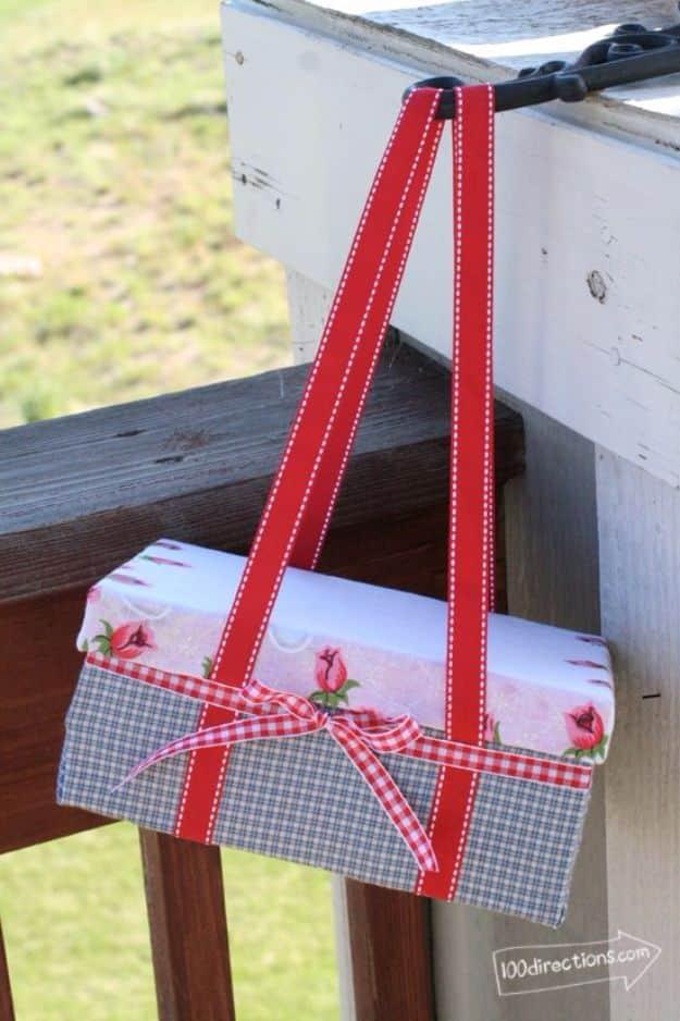 Shoe box covered in gingham and floral paper with red ribbon handles and a bow, sitting on a wooden railing