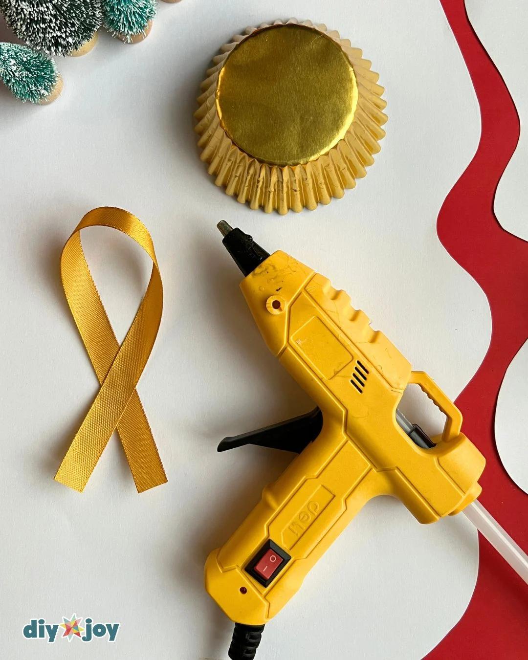 DIY Christmas ornaments supply flat lay with gold cupcake liners, ribbon and a hot glue gun on a white table