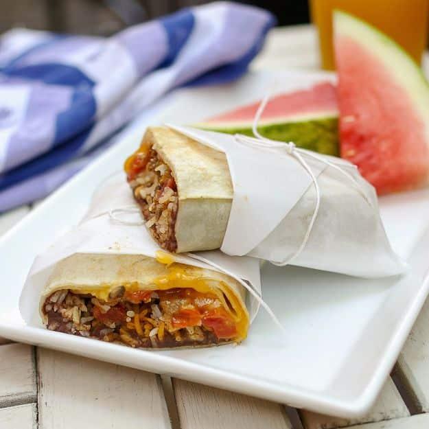 Beef and mushroom burritos wrapped in parchment and tied with string on a white plate with watermelon