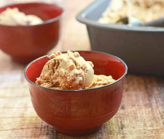 No churn coffee brickle ice cream scooped into two red bowls with toffee bits, loaf pan behind on a wood table