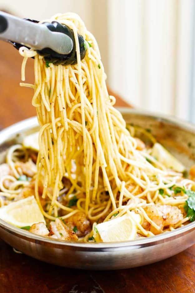 Garlic butter shrimp pasta being lifted with tongs from a stainless pan, spaghetti with shrimp and lemon