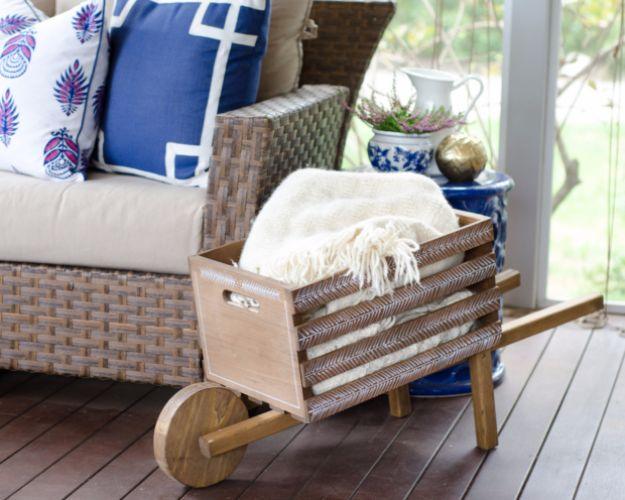 A small decorative wooden wheelbarrow in weathered gray sits on a front porch filled with pumpkins and greenery