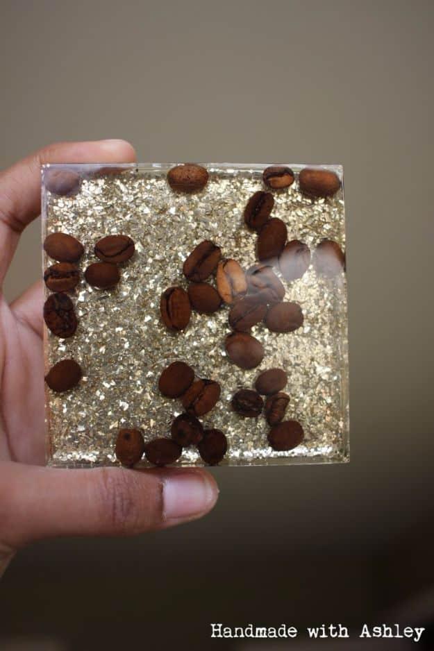DIY resin coffee bean coaster, a clear square resin coaster with whole coffee beans and gold glitter suspended inside