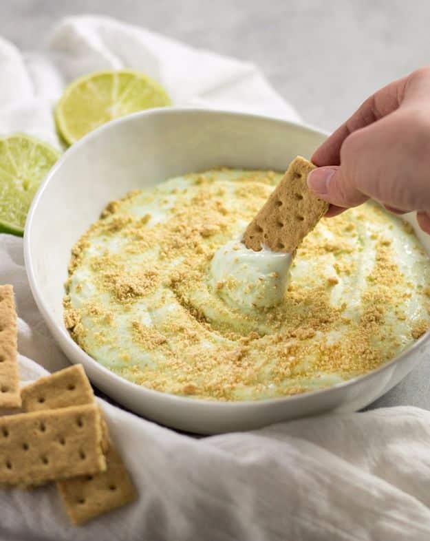 Key lime pie cheesecake dip in a bowl with lime zest on top, served with graham crackers for dipping