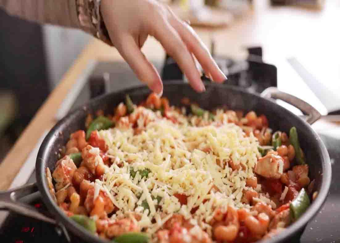 Adding grated cheddar cheese over the pasta