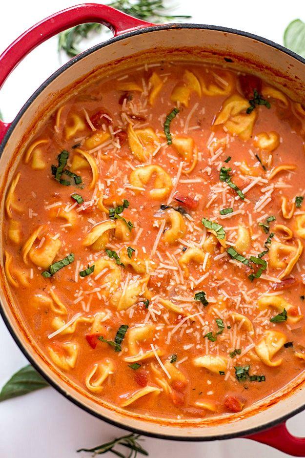 One pot creamy tomato tortellini soup in a red Dutch oven, cheese tortellini under grated Parmesan and basil