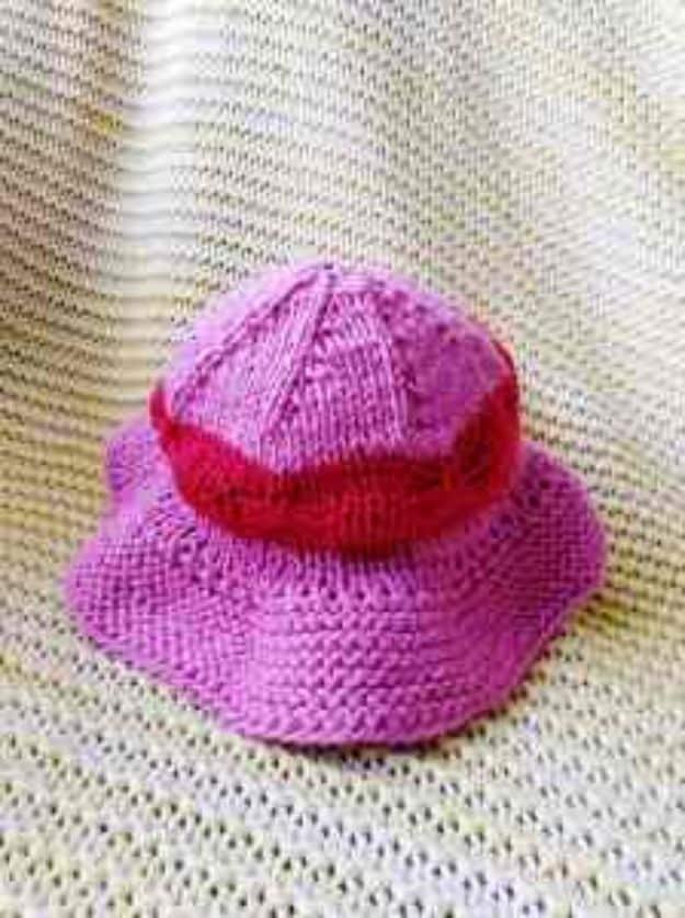Bright pink knitted baby sun hat with a turned up brim and darker pink band, resting on a pale knitted blanket