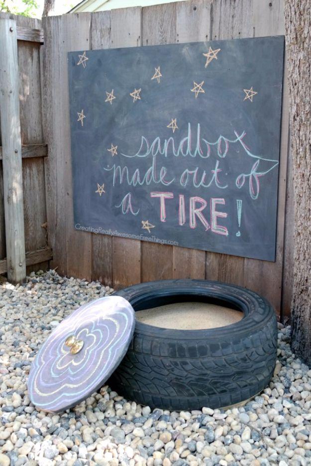 Old tire sandbox filled with sand with a round chalkboard painted plywood lid and doorknob handle beside it