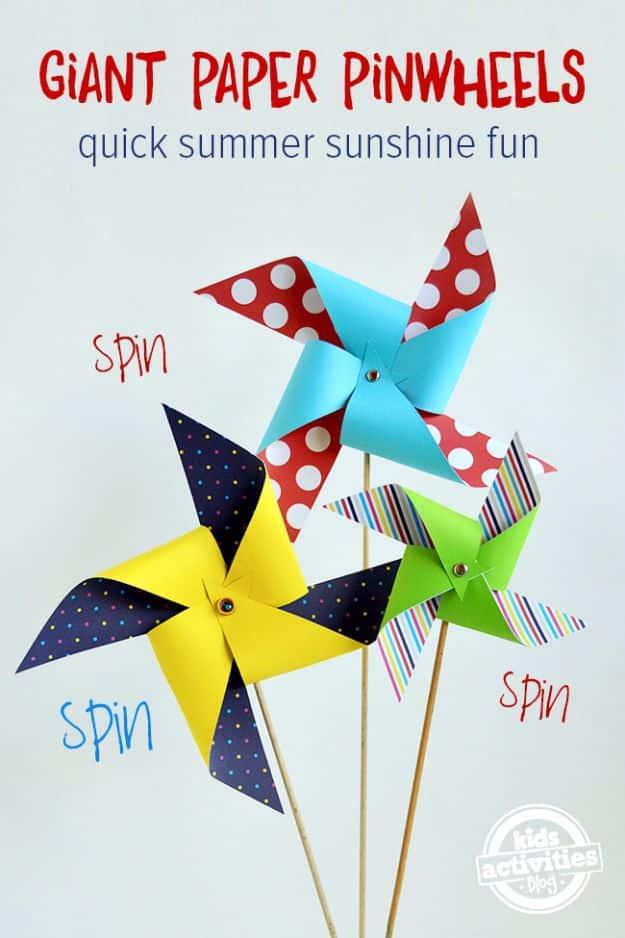 Three giant paper pinwheels in red spotted, yellow and green striped paper on wooden dowels against a pale background