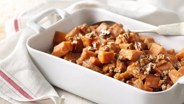 Orange sweet-potato cubes topped with chopped nuts in a white rectangular serving dish for a holiday side