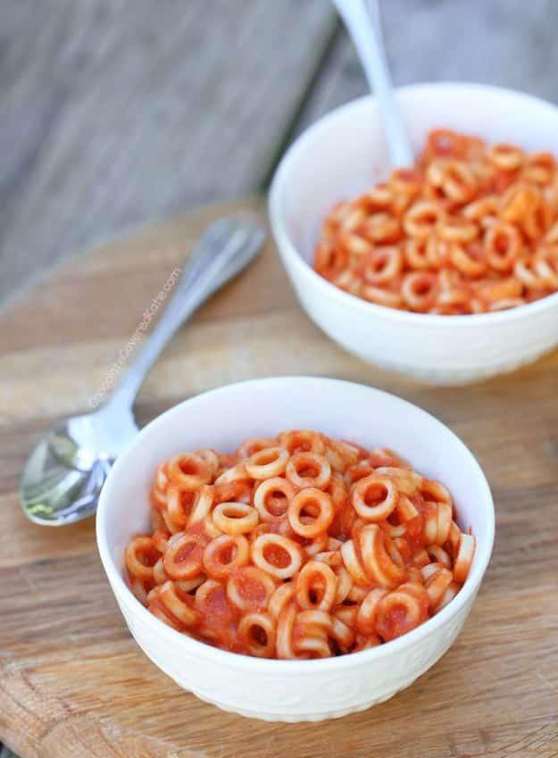 Homemade spaghetti os in two white bowls, small ring pasta in an orange tomato sauce on a wooden table