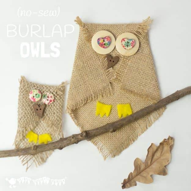 Two burlap owls with wooden button eyes and yellow felt feet perched on a bare branch beside a dried oak leaf