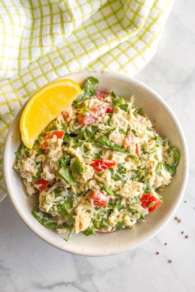 Tuna spinach salad in a white bowl with flaked tuna, chopped baby spinach, red tomato and a lemon wedge