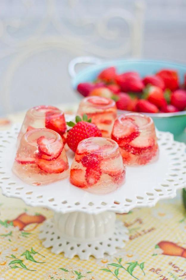 Champagne strawberry jello shots unmolded onto a plate with sliced fresh strawberries suspended inside