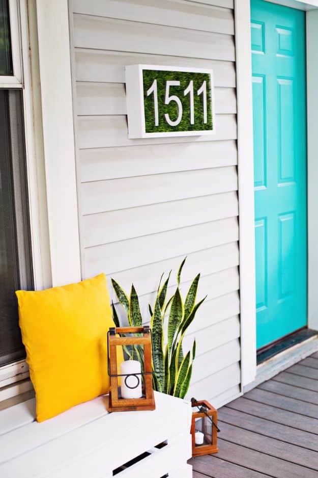 Modern DIY house number plaque with white numerals on a green ground, mounted beside a teal front door