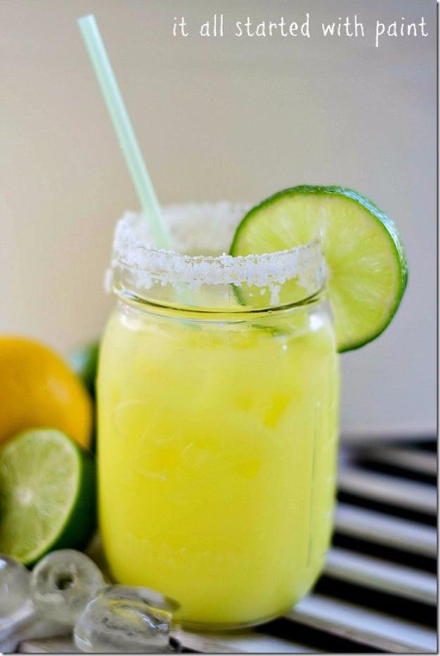 Salt rimmed mason jar of pale yellow margarita with a lime wheel and a drinking straw on a metal surface