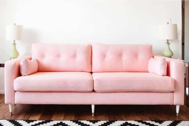 Pale pink tufted midcentury sofa with gold and white tapered legs, green lamps and a black and white chevron rug