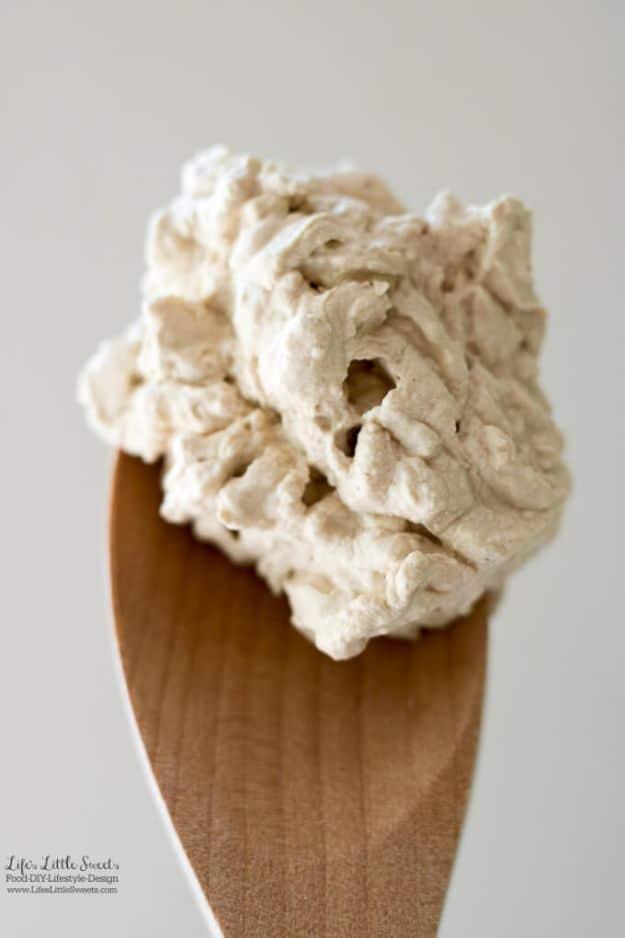 Soft tan swirl of coffee whipped cream piled high on a wooden spoon against a plain white background