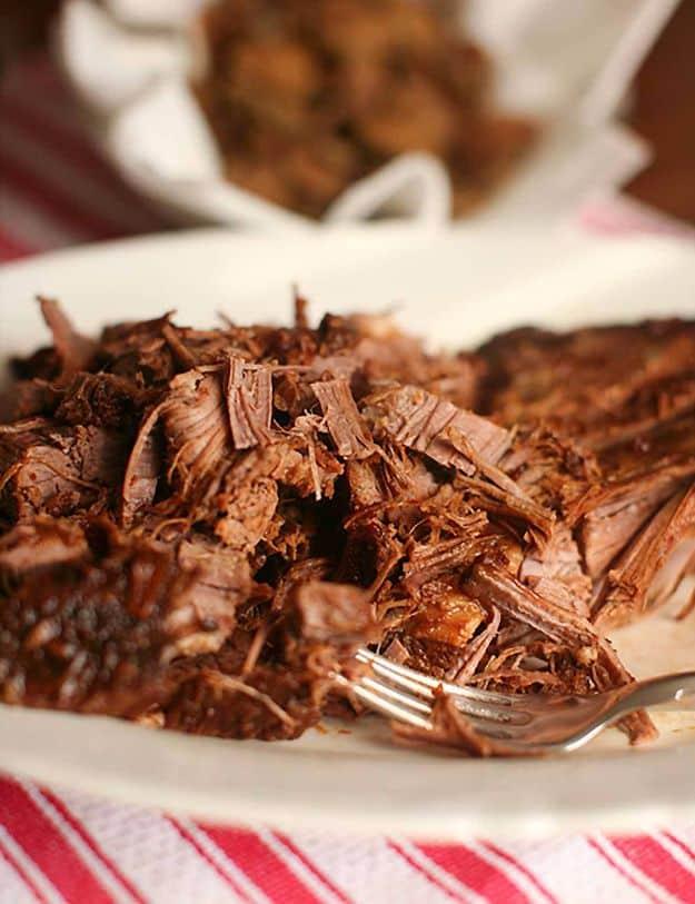 Coca Cola brisket sliced and shredded onto a white plate resting on a red and white striped kitchen cloth