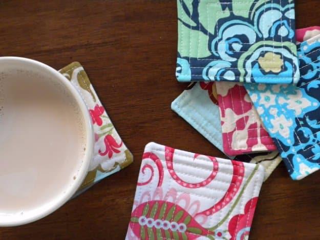 A stack of four quilted coasters in mixed cotton prints beside a striped mug, small sewn items that sell all year round.