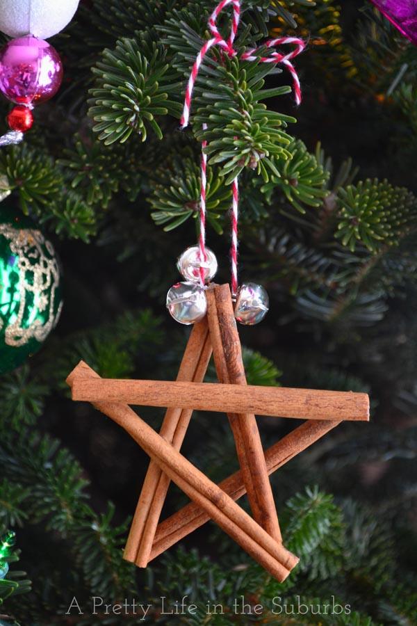 A star ornament of five cinnamon sticks with three silver bells and red and white twine hanging on a real Christmas tree