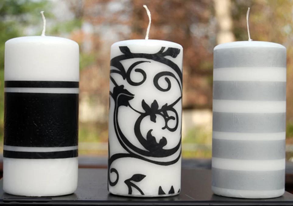 Three white pillar candles with black bands, a black damask scroll and gray stripes standing on a dark table outdoors