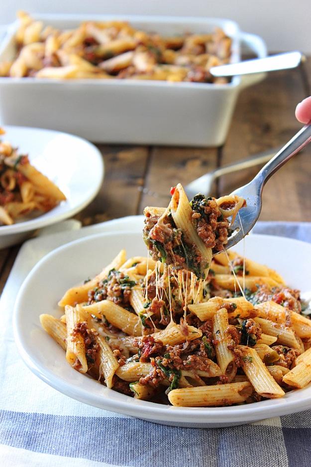 Slow cooker beef and cheese penne with spinach in a white bowl, a fork lifting out a bite with a cheese pull