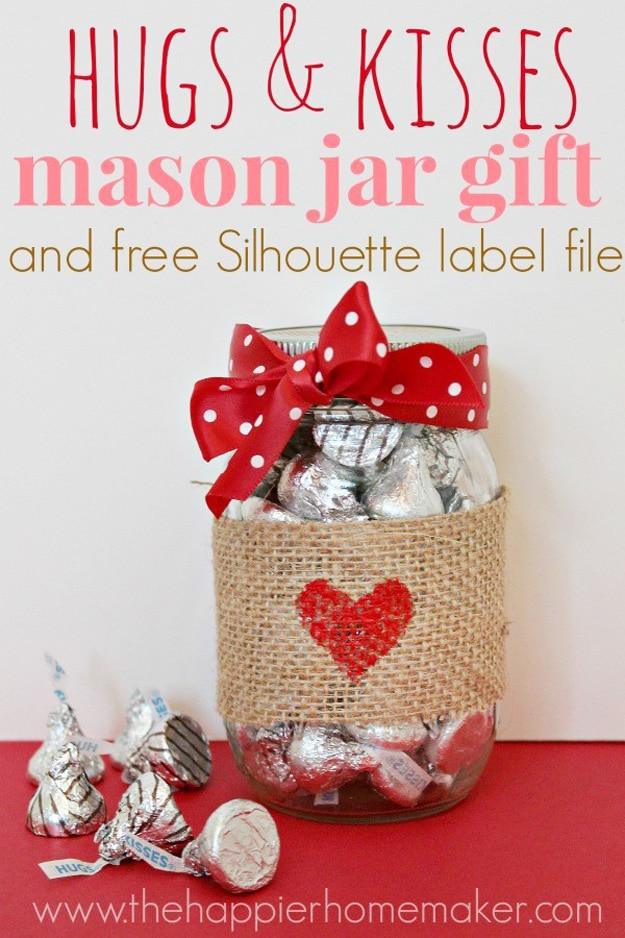 Mason jar filled with foil wrapped chocolate kisses and a printable hugs and kisses Valentine label on a craft table