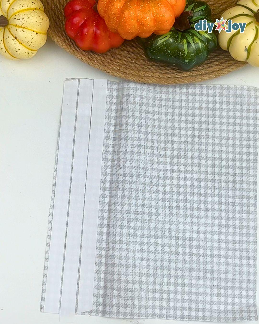 No Sew Crafts - gray gingham fabric laid right side down with two vertical strips of double-sided tape along the left edge