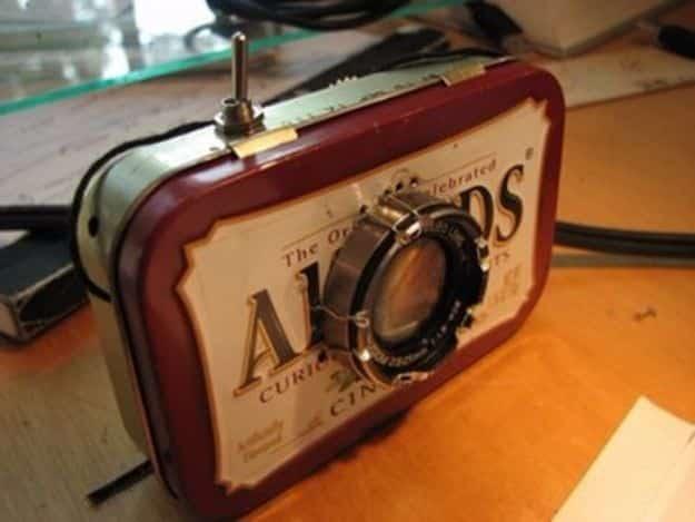 Palm sized homemade film projector built into a small Altoids tin with lenses and film reels on a wooden desk