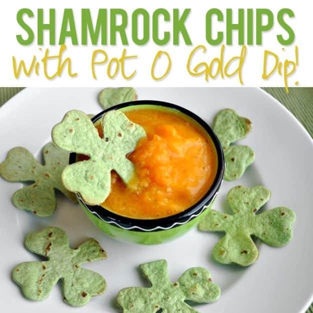 Green tortilla shamrock chips on a white plate around a bright green bowl of smooth golden yellow dip