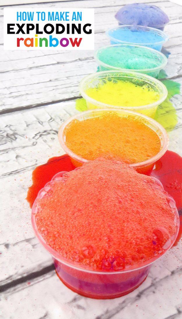 Exploding rainbow, six clear cups in a row on white wood, each overflowing with red, orange, yellow, green and blue foam