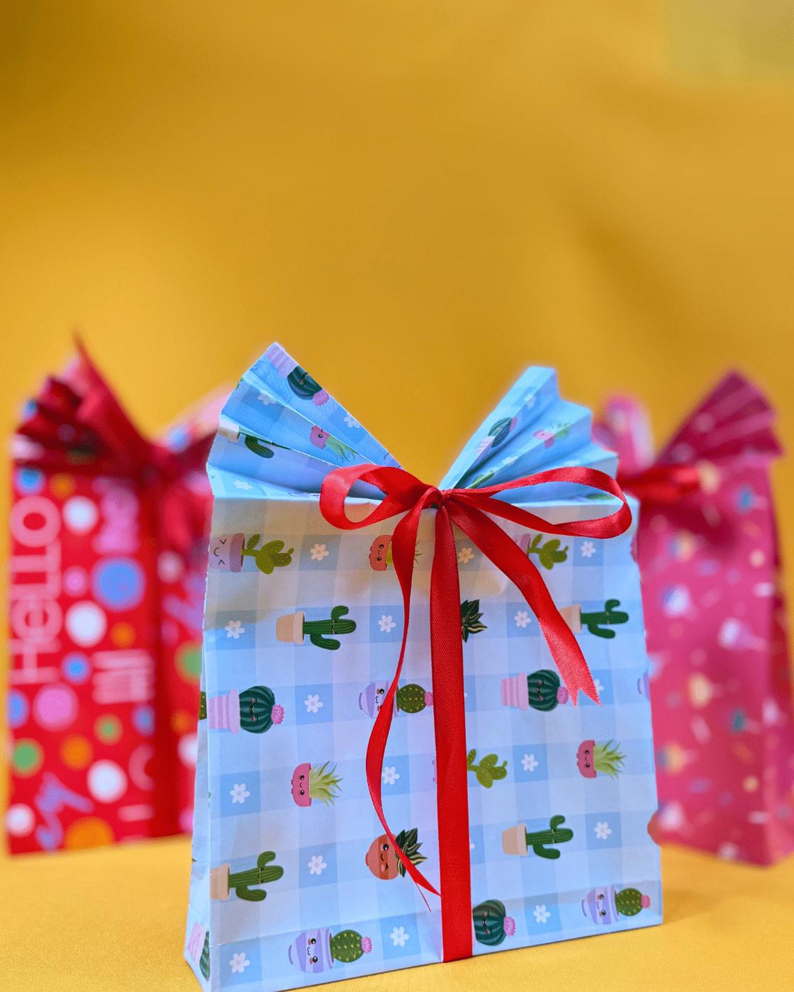 Holiday Gift Bags - close up of a cactus print paper gift bag with a pleated top and red bow