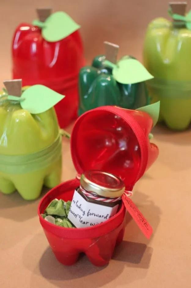 Five apple shaped containers made from plastic bottle bottoms spray painted red and green, one open with a gift jar