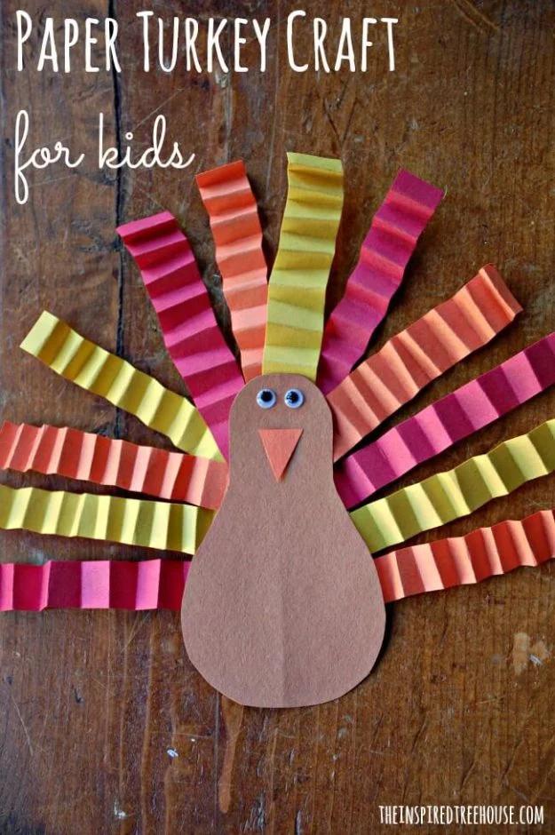 Paper turkey with a brown body and accordion folded yellow, orange and pink feathers fanned out, on dark wood