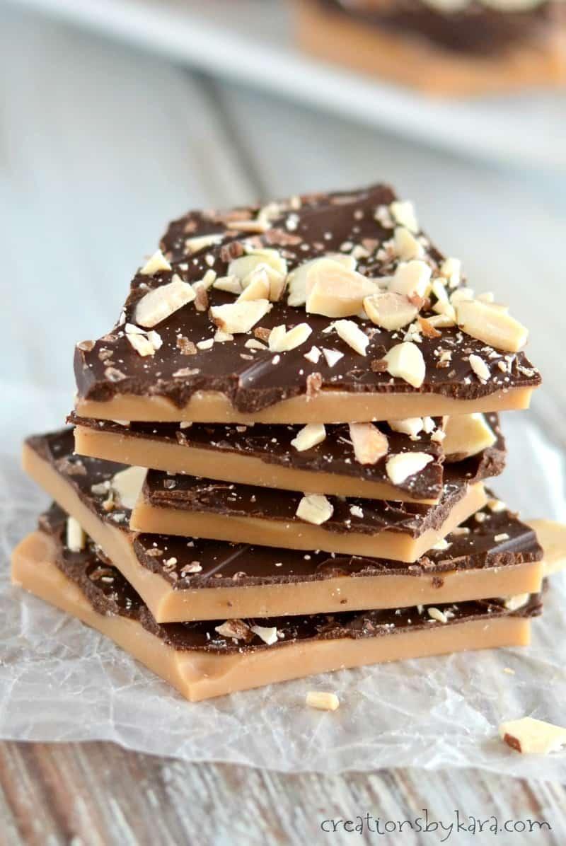 Stack of broken English toffee shards topped with dark chocolate and chopped almonds on crumpled parchment