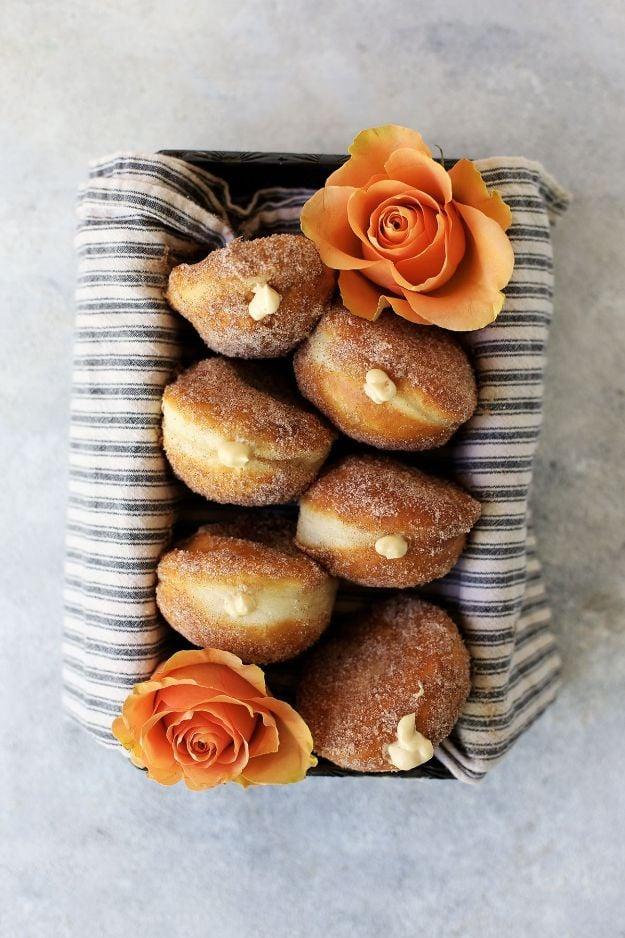 Salted caramel cream cheese filled donuts rolled in cinnamon sugar, stacked in a striped paper baking tray