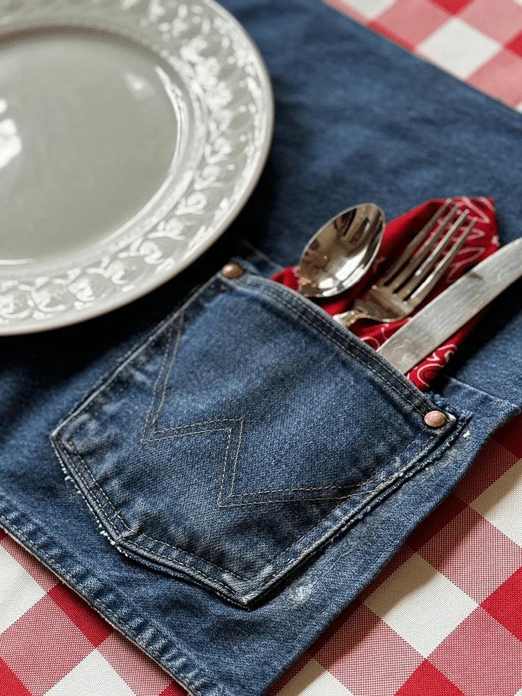A placemat sewn from recycled denim with the jeans back pocket holding a fork and knife on a wood table