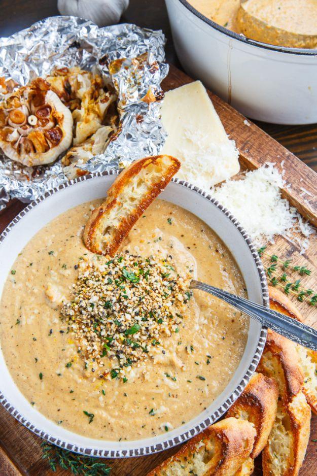 Asiago roasted garlic cauliflower soup in a bowl with a crunchy seed topping, foil wrapped garlic beside