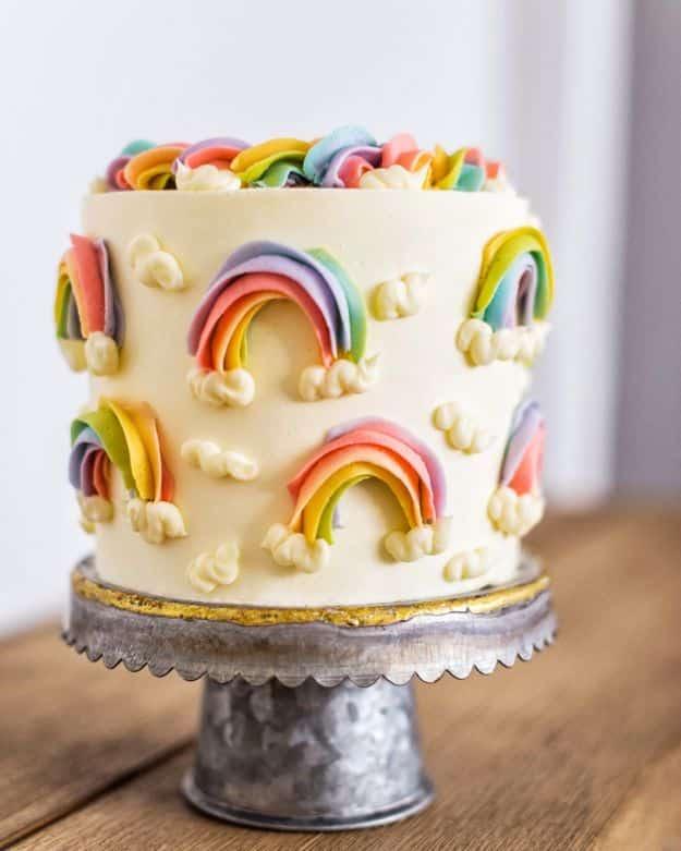 Birthday cake piped with buttercream rainbows and white clouds around the sides and a braided rainbow border on top