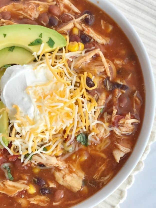 Taco ranch chicken chili in a white bowl topped with avocado slices, sour cream and shredded jack cheese