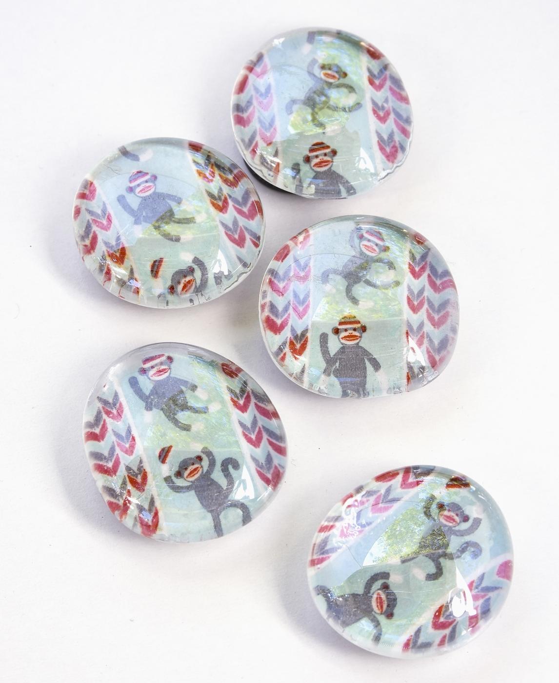 Five round glass marble magnets showing patterned washi tape and paper through the glass on a white surface