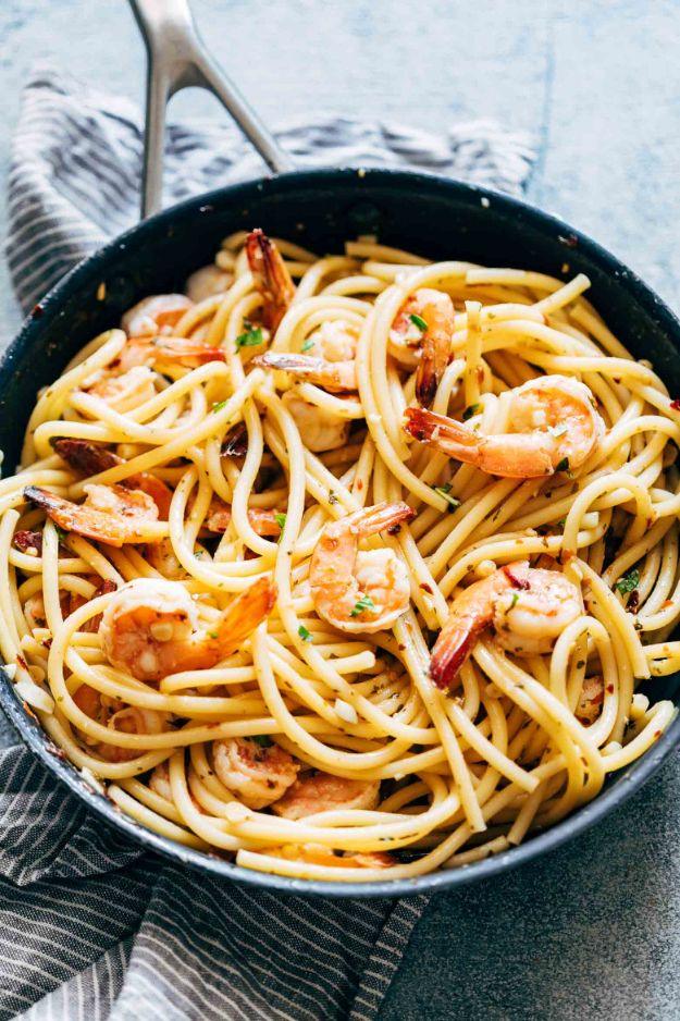 Shrimp spaghetti aglio olio in a dark pan, long spaghetti with chilli flakes and whole shrimp tossed through