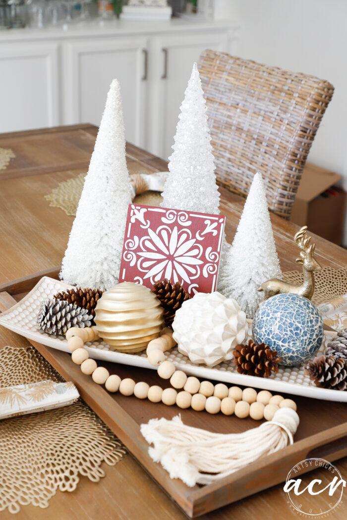 Red dollar store sign with a raised white stenciled snowflake pattern beside gold glitter snowflakes hanging on fishing line