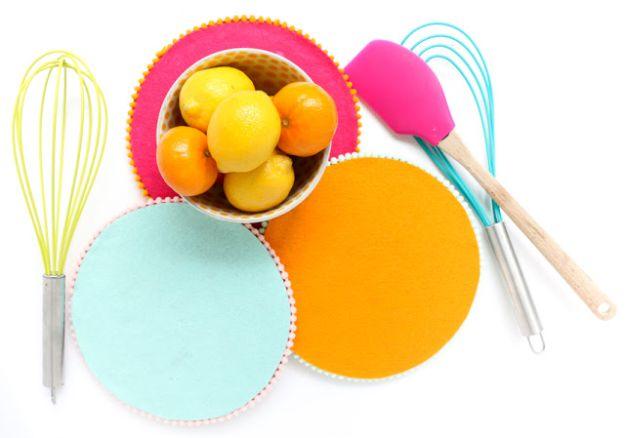 Mint, orange and pink felt covered cork trivets with pom pom trim, photographed with whisks and a bowl of lemons