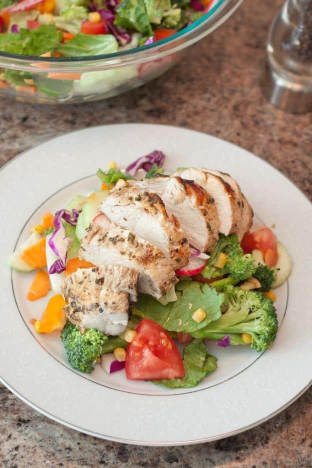 Mediterranean grilled chicken breast sliced over a garden salad with tomato, broccoli and corn on a white plate