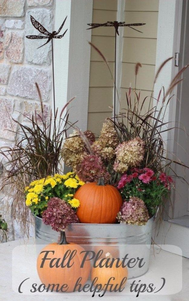 Galvanized tub planter on a porch with purple fountain grass, dried hydrangeas, yellow mums and an orange pumpkin