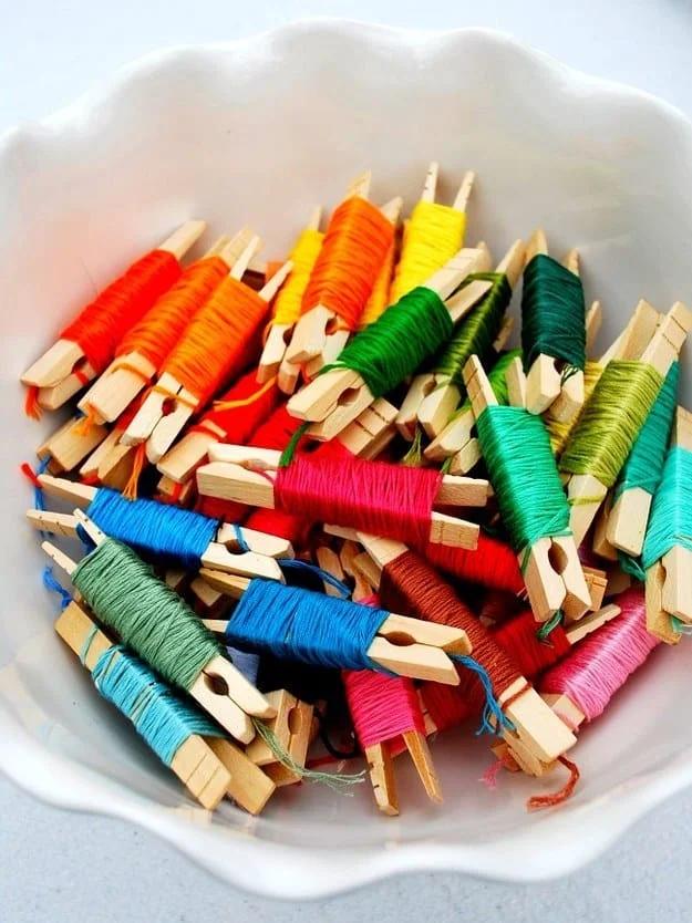 Embroidery floss in rainbow colors wound onto wooden clothespins, piled in a white scalloped dish on a table