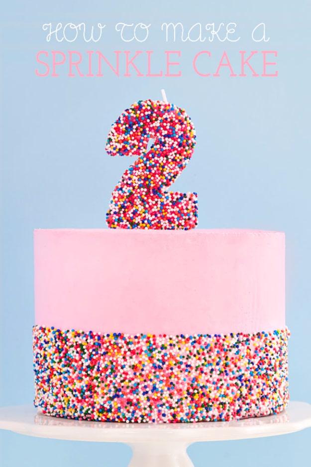 Pink layer cake with a thick rainbow sprinkle band around the base and a sprinkle covered number two on top